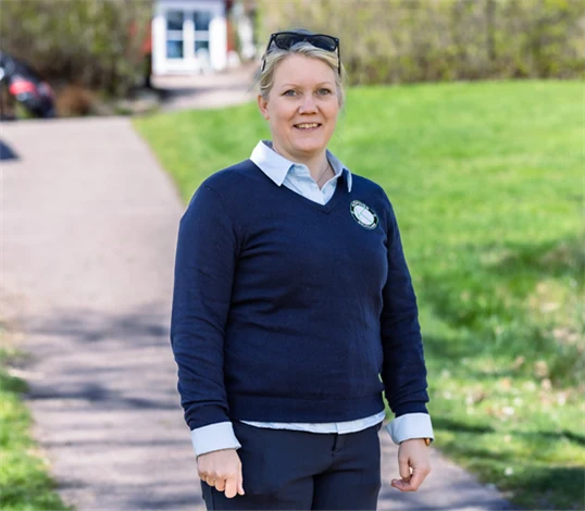 Bild på Lena Björkdahl som är klubbchef för Köpings Golfklubb. Hon står utomhus utanför golfklubben.
